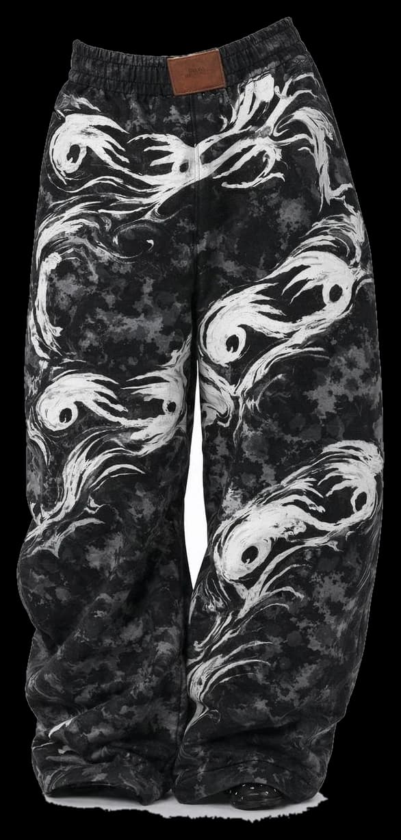 The Ishiki Pants — wide-legged black trousers with a mottled wash and large white brushed graphics down both legs.