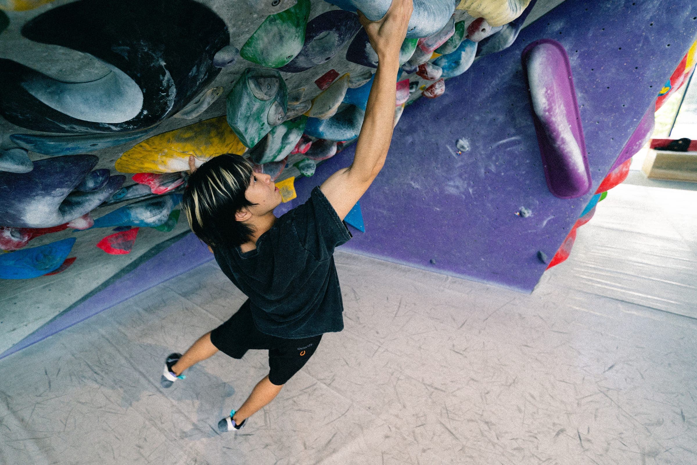 A climber reaching for a high hold on a steep overhang, seen from above.