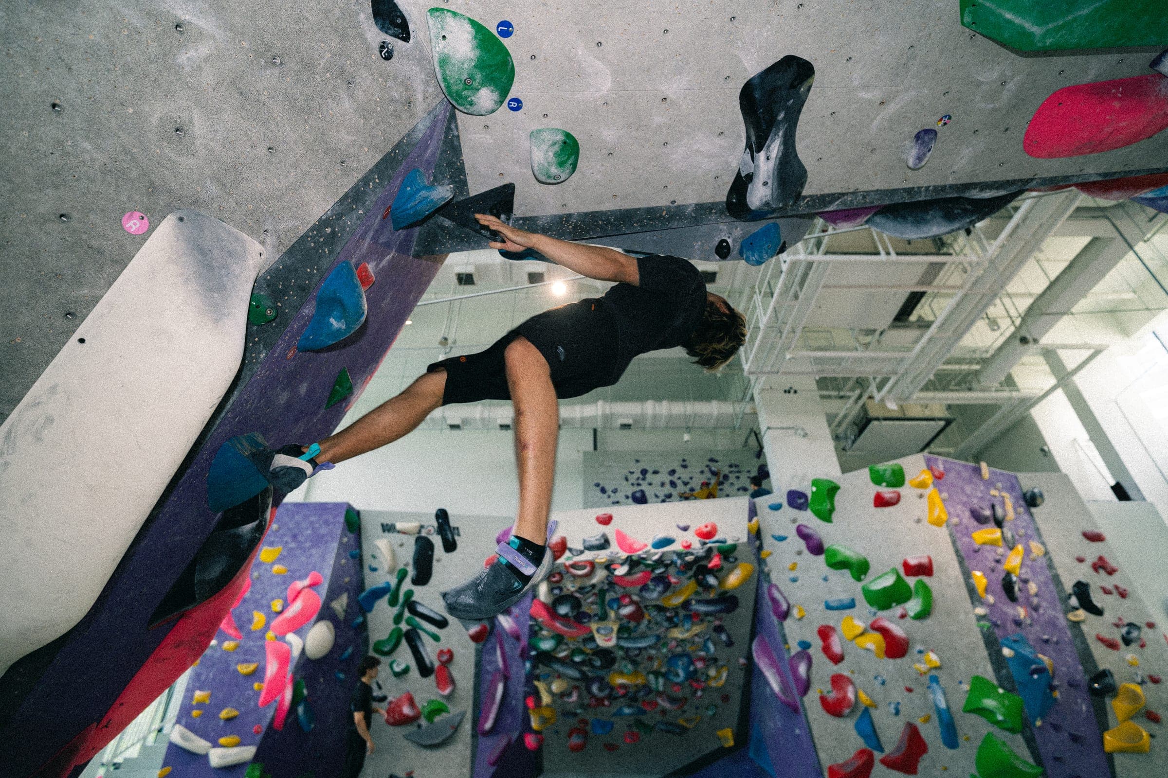 A climber stretched horizontally beneath a roof, the gym floor far below.